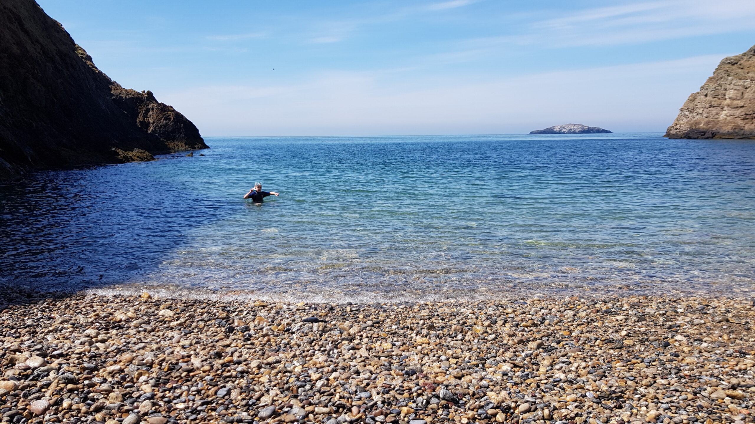 A cove with a child using a snorkel on Anglesey coastal path